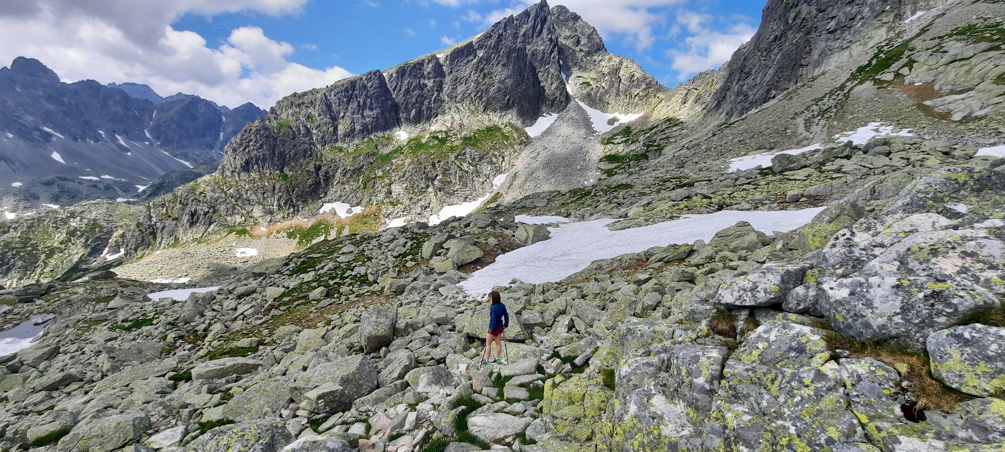 Všechno zvládnete? Horská krajina se skalami a sněhem, v dálce turistka na stezce